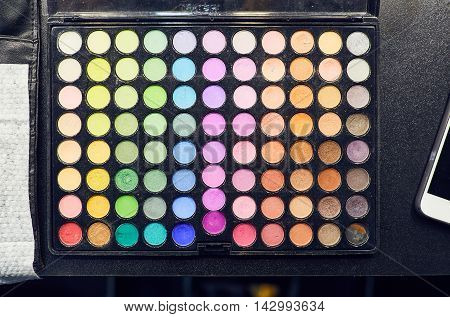 Top view makeup colorful eyeshadow palettes on the table. Large eyeshadow makeup palette on black background. Close up colorful eye shadow make up.