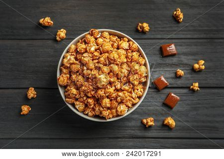 Delicious Popcorn With Caramel In Bowl And Candies On Wooden Background, Top View