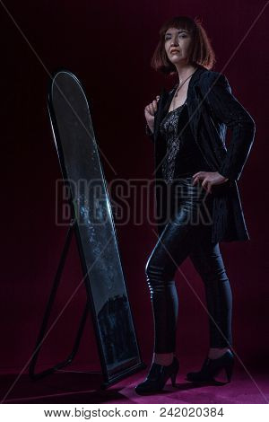Confident Ugly Woman Wearing Black Suit Stands Near Mirrow In Front Of Camera On Stage With Crimson 