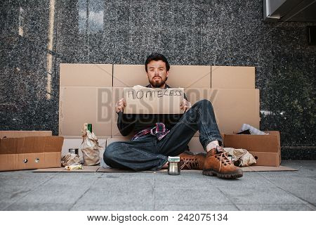 A Picture Of Dirty Man Sitting On Cardboard And Looking Straight. He Is Tired And Exhausted. Guy Is 