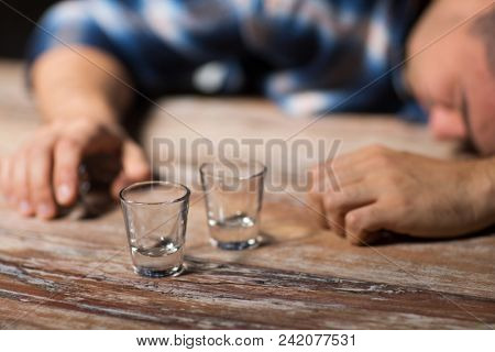 alcoholism, alcohol addiction and people concept - male alcoholic with empty glasses lying or sleeping on table at night