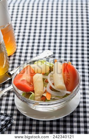 A Salad Inside A Glass Bowl And Placed On A Black And White Checkered Tablecloth.