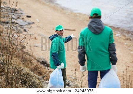 One of greenpeacers pointing at coastline and offering his colleague to clean that territory