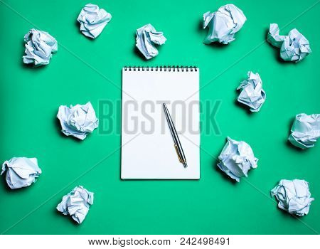 White Notebook With Pen On A Green Background Among Paper Balls. The Concept Of Generating Ideas, In