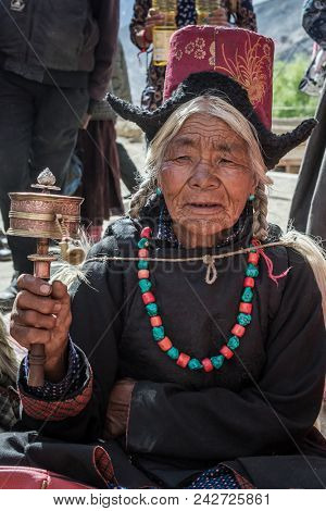 Lamayuru, India - June 19, 2017: Unidentified ladakhi old lady with the tibetan prayer wheel during buddhist festival in Lamayuru Gompa monastery, Ladakh, Northern India