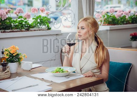 Blonde Woman Having Lunch At The Restautant. Beautiful Woman Drink Red Wine And Waiting Somebody