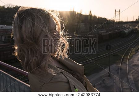 Attractive Young Caucasian Blonde Woman In Trench Walking In City With Vintage Suitcase Above Railwa