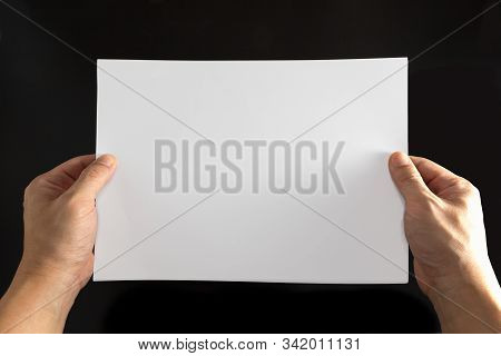 The Concept Of Both Hands That Holds A White Sheet Of Paper On A Black Background.