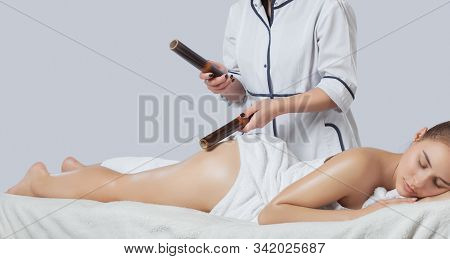 Masseur Makes Anti-cellulite Massage With Bamboo Sticks On Thighs, Legs And Buttocks In A Beauty Sal
