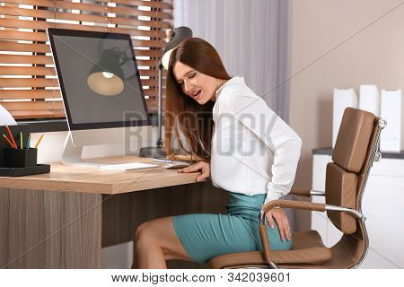 Young Woman Suffering From Hemorrhoid At Workplace In Office