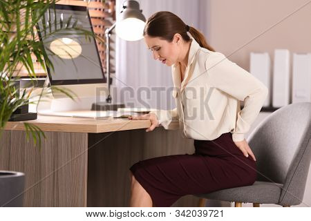 Young Woman Suffering From Hemorrhoid At Workplace In Office