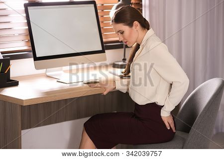 Young Woman Suffering From Hemorrhoid At Workplace In Office