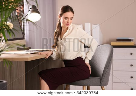 Young Woman Suffering From Hemorrhoid At Workplace In Office