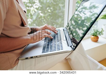 Cropped Image Of Woman Sitting On Window Sill At Home And Working On Laptop