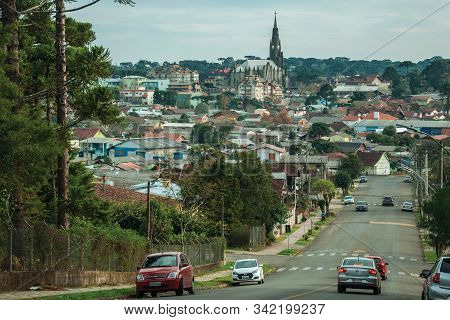 Canela, Brazil - July 21, 2019. Street With Cars Going Towards Cityscape Of Houses And Church Steepl