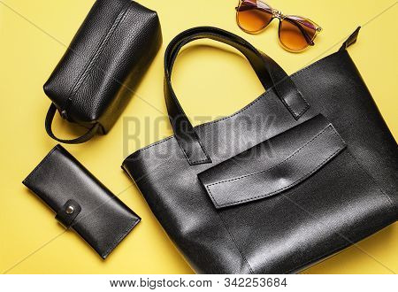 Black Fashion Leather Accessories, Wallet, Cosmetic Bag And Sungasses On Yellow Background, Flat Lay