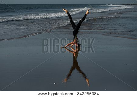 Yoga Headstand Variation Sea Background. A woman performing a headstand on beach in the sea