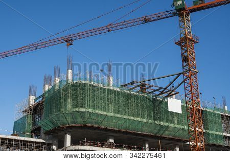 Crane And Building Construction Site Against Blue Sky. Metal Construction Of Unfinished Building On 