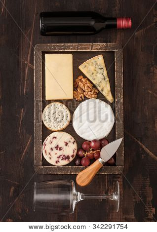 Glass And Bottle Of Red Wine With Selection Of Various Cheese In Wooden Box And Grapes On Wooden Bac