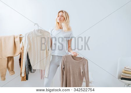 Eternal Question.blond Depressed Thoughtful Female Standing Near Wardrobe Rack With Clothes, Having 