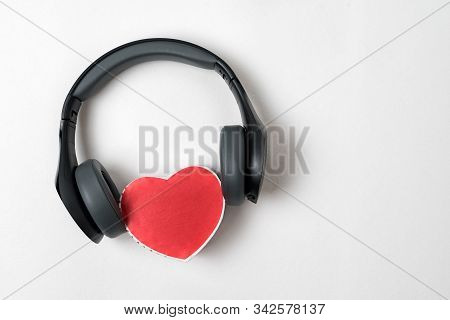 Full-size Wireless Headphones Pulled Over Small Red Heart-shaped Box On White Table. Love Music Conc
