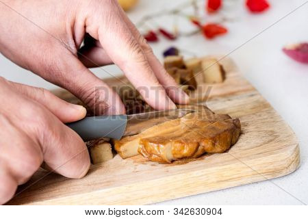 closeup of a cauacsian man cutting a piece of seitan into strips on a wooden cutting board, on a white stone countertop