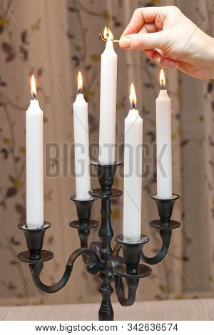 Burning Candles In Retro Candlestick Stands On Table In Room. Woman Hand Lights Candles. Romantic At
