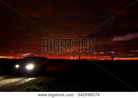 A Car In Front Of A Red Sunset By Cloudy Weather