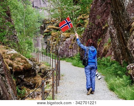 Tourist Woman With Norwegian Flag And Camera Walking Trough Mountains Path In Allmannajuvet Area Sau