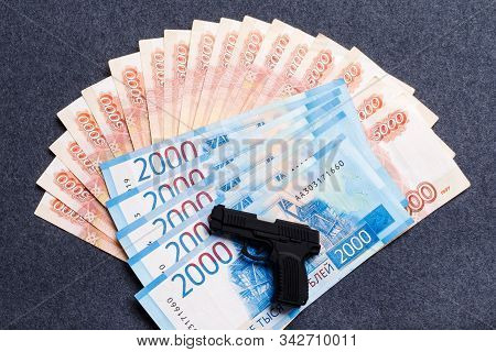 A Small Toy Gun Lies On A Monetary Background Of Five Thousandths And Two Thousandths Of Russian Rub