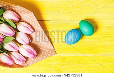 Easter Is Coming. Colorful Bright Eggs And Bouquet Fresh Tulip Flowers On Yellow Background Top View