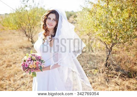 Beautiful Smiling Bride Wearing A Natural Flower Wreath And Standing In The Golden Summer Fields Wit