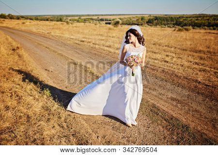 Beautiful Smiling Bride Wearing A Natural Flower Wreath And Standing In The Golden Summer Fields Wit