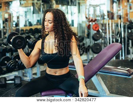 Stock Photo Of A Black Girl Sitting In The Gym Surrounded By Weights And Mirrors