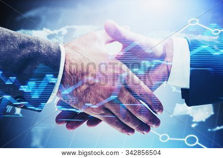 Close Up Of Two Businessmen Shaking Hands Over Blue Background With Double Exposure Of Blurry Graph 