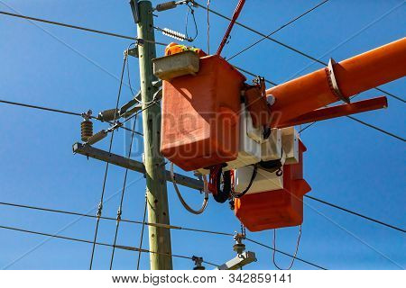 A Low Angle Shot Of A Man At Work In Bright Orange Aerial Work Platform, Cherry Picker, Servicing An