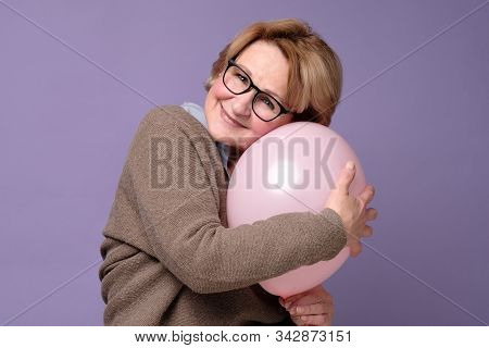 Caucasian Senior Woman In Glasses And Sweater Hugging Pink Balloon