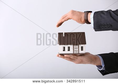 Insurance Agent With Model Of House On Light Background. Protection Of House From Earthquake