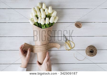 Woman Florist Wrapping Beautiful Bouquet Of White Tulips In Pack Craft Paper On The Wooden Table. Fl
