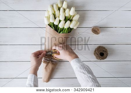 Woman Florist Wrapping Beautiful Bouquet Of White Tulips In Pack Craft Paper On The Wooden Table. Fl