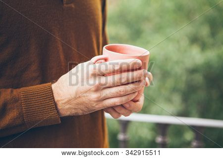 Close-up Of Man Hands Holding Ceramic Cup Of Tea / Hot Beverage While Standing On The Balcony With G