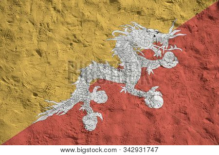 Bhutan Flag Depicted In Bright Paint Colors On Old Relief Plastering Wall. Textured Banner On Rough 