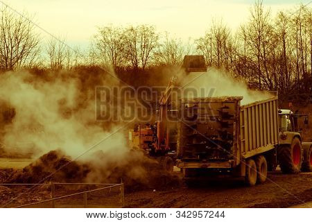 Excavator Loads Manure, Hovering In The Cold Air, Into A Tractor With A Trailer. Late Fall. Vintage 