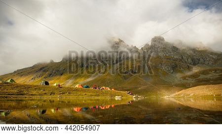 Tent On The Shore Of A Mountain Lake Framed By Rocky Mountains. Russia, Arkhyz