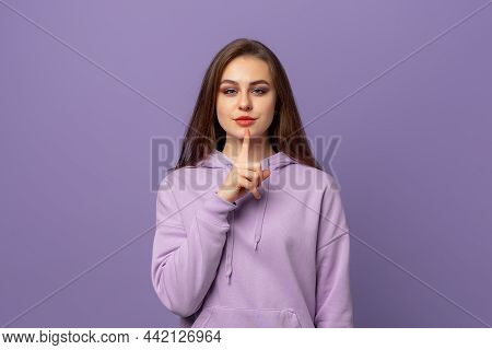Portrait Of Beautiful Young European Woman With Chestnut Hair Holding Index Finger At Lips, Asking T