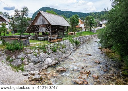 The Bank Of Mostnica River In Stara Fuzina Village In Slovenia, With A Kozolec Hayrack, At Dusk.