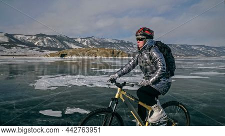 Woman Is Riding Bicycle On The Ice. Tires On Bike Are Covered Wi