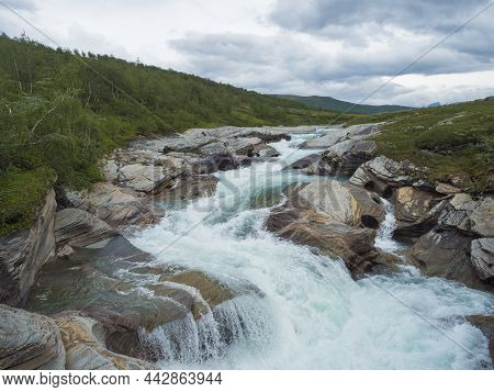 Milky Blue Glacial Laddejahka River Rapids With Colorful Stones In Lapland Landscape With Green Moun