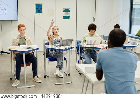 Diverse Group Of Chilrden Sitting At Desks In Modern School Classroom Focus On Teenage Girl Raising 