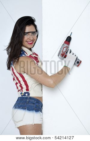 High fashion glamour model in Daisy duke shorts, tool belt, red bra with a screw gun 